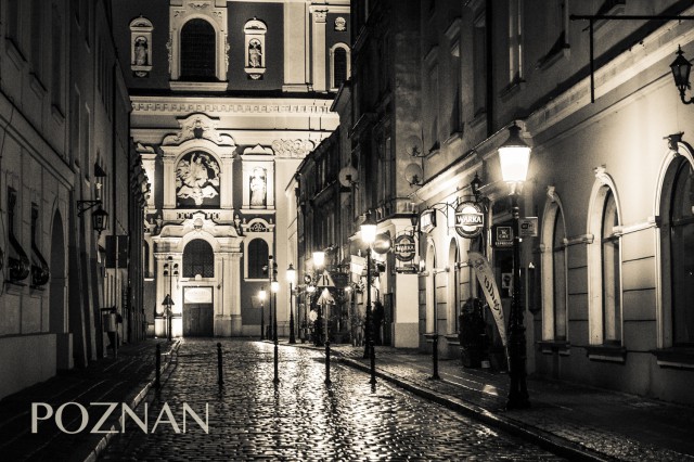 Black and White Photo of old buildings lit by street lamps in Poznan