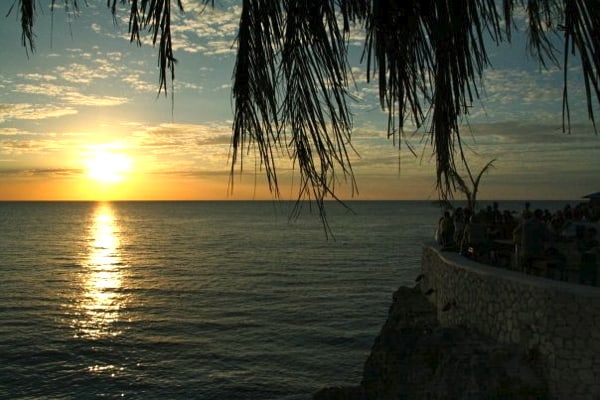 Yellow sunset with blue sky with a Palm tree and stone wall