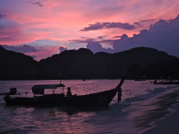 very pink sunset with a shadowed boat and mountain over water