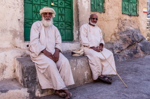 Two old Omani men sat outside of a house. They are sat on traditional external steps to most Arab houses
