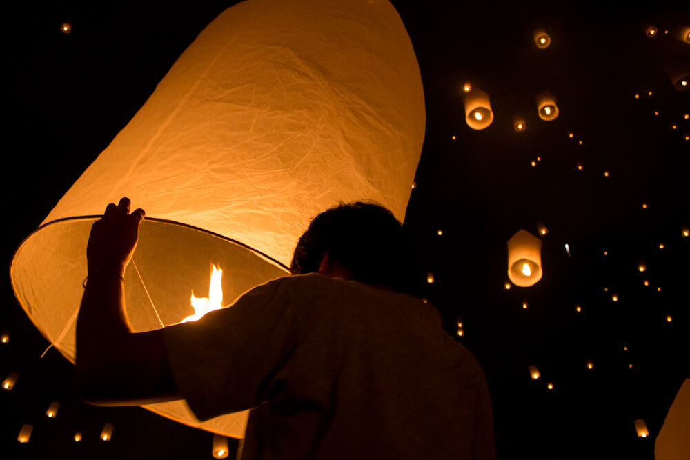 Mann zündet Papierlaterne beim Yee Peng Festival in Thailand an