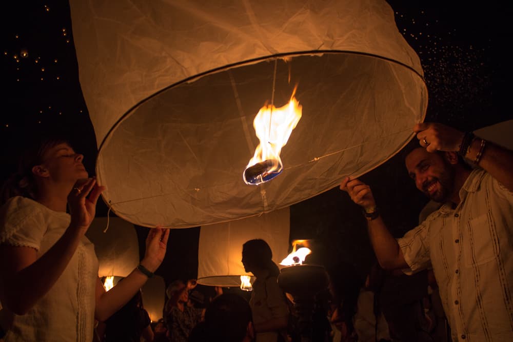 Mann zündet beim Yee Peng Festival in Thailand mit anderen Menschen um ihn herum eine Papierlaterne an
