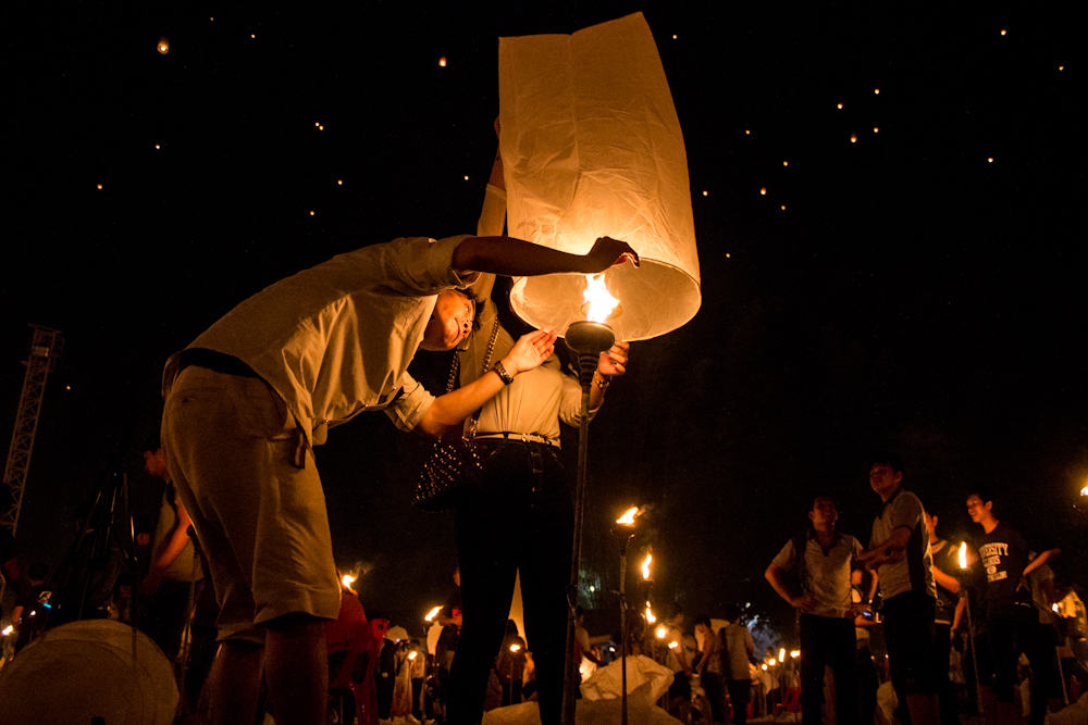 Mann zündet beim Yee Peng Festival in Thailand mit anderen Menschen um ihn herum eine Papierlaterne an