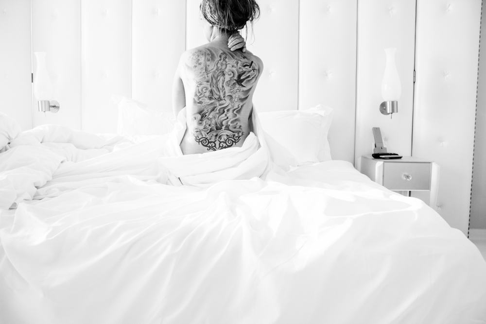 Woman sitting in a hotel bed showing the tattoo on her back