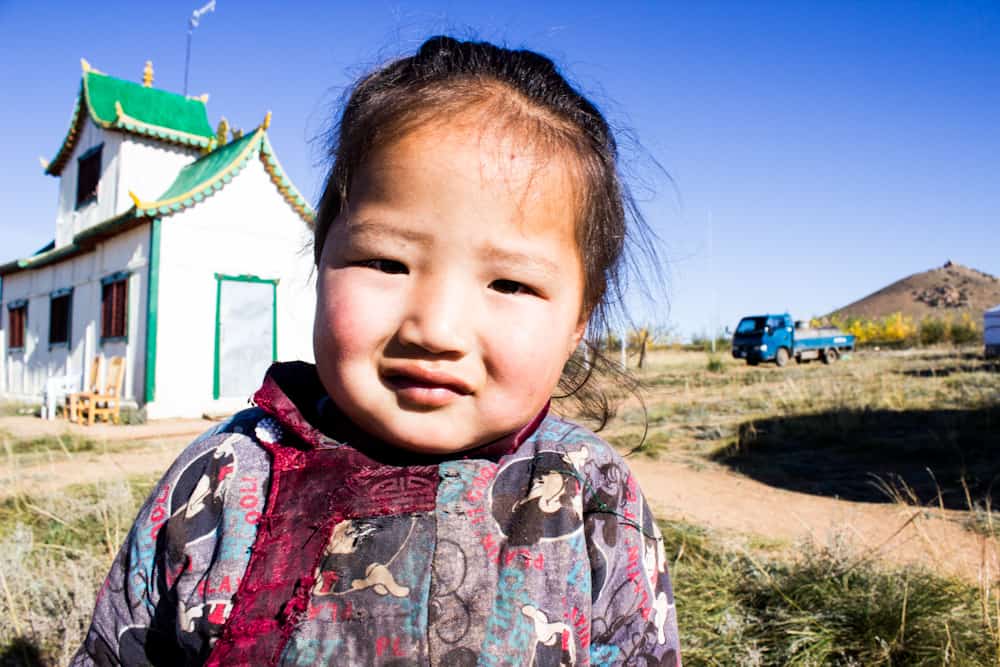 small girl smiles at the camera with a house behind her