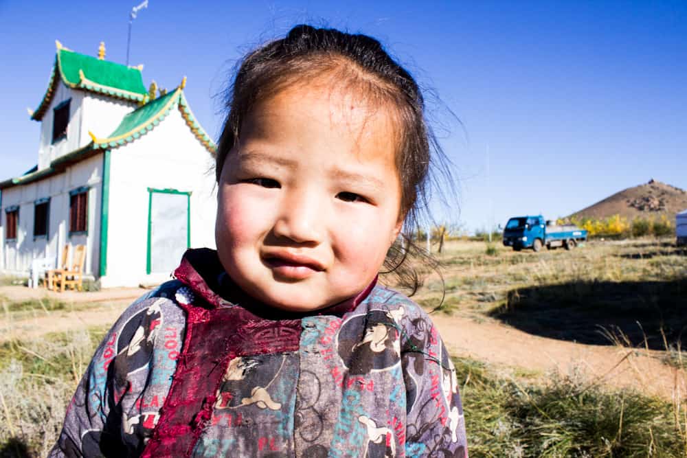 small girl smiles at the camera with a house behind her