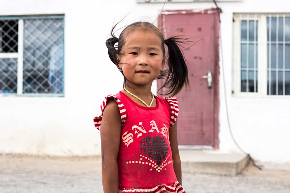 small girl with pigtails smiles at the camera as on of the faces of Mongolia