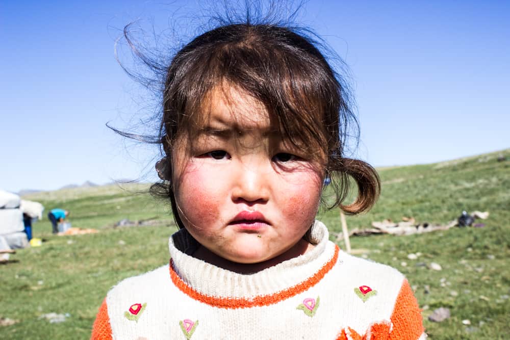 small girl with her hair blowing in the wind in a orange sweater with flowers