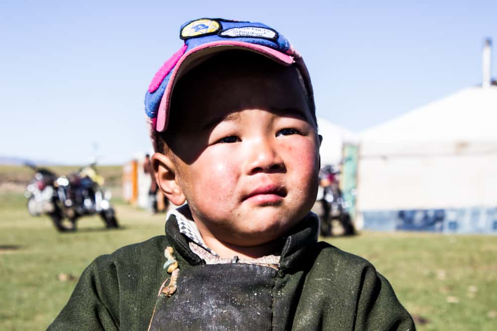 small boy smiles at the camera with a house behind her