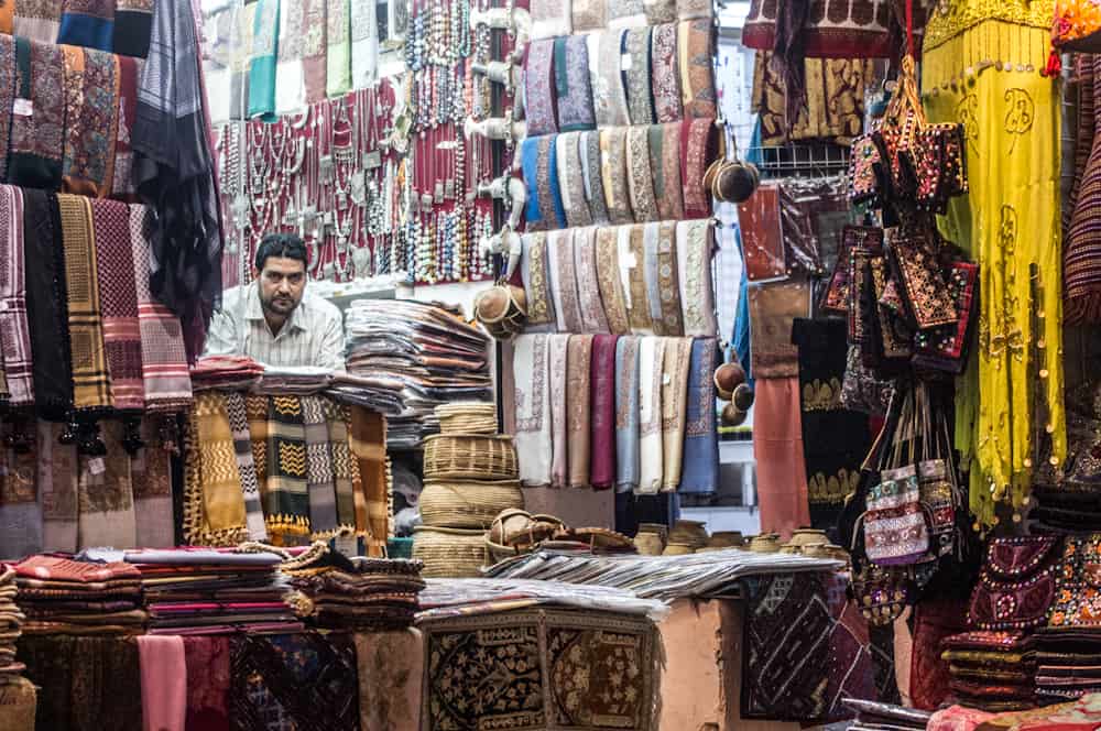 frowning man in a market booth selling scarves and jewelry