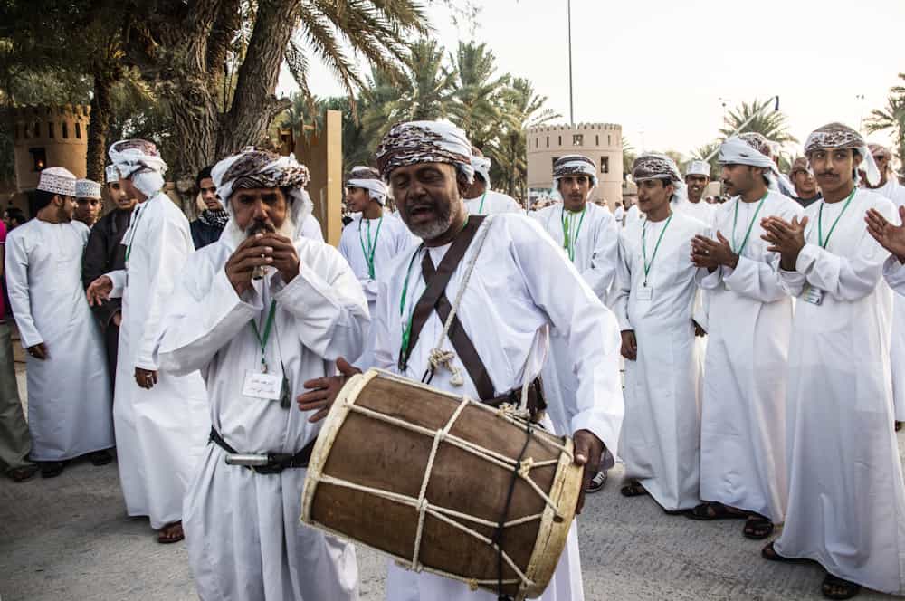 men in all white clothing in a parade with one man playing the drums and one playing the flute