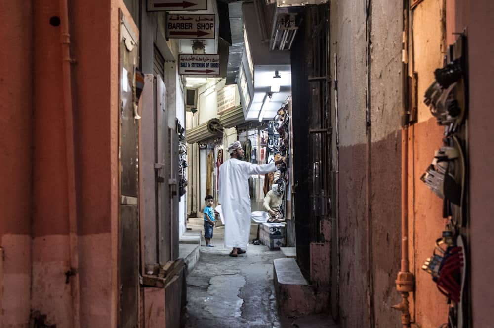 muscat oman muttrah souk man dressed in white traditional clothing next to a small boy in a market alley in Muskat, Oman