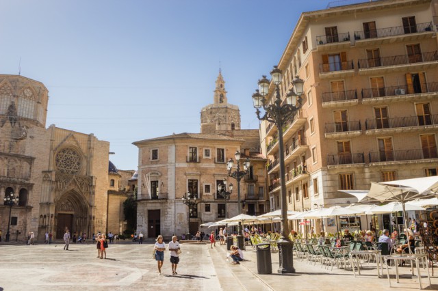 old town square of Valencia with people walking around and eating at a patio with a old church in the background