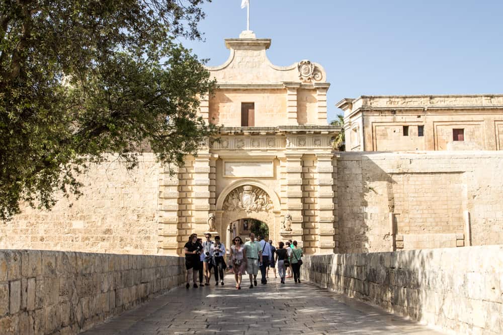 Bridge with people walking across with large gate behind them as pictured in Game of Thrones Malta Mdina KIng's Landing