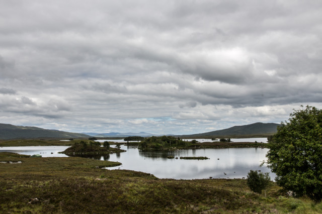 Glencoe Valley in Scotland with a shallow river surrounded by low moutains and bushes