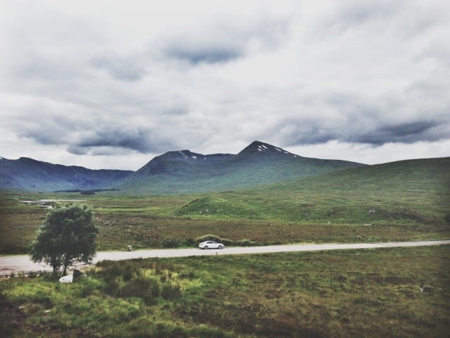 Blue Mountain Landscape with a cloudy sky with a white car on the road driving through 5 days in Scotland Roadtrip