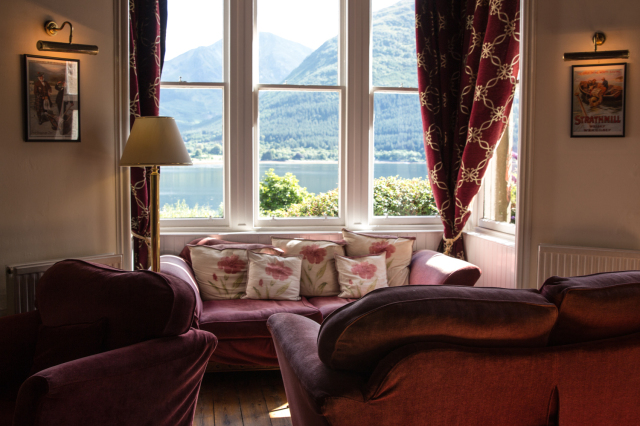 Red Coach with flower pillow with a beautiful Scotland landscape behind of mountains and a lake