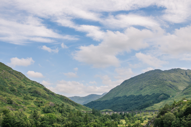 Glennfinnan Viaduct shown among green mountains and a blue sky 