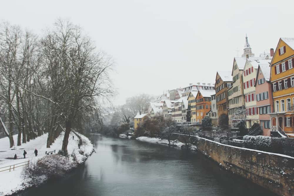 old german town in winter with a snow covered park, river and colorful houses.