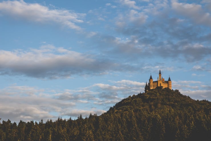 castle on top of a mountain, covered in green trees with blue sky