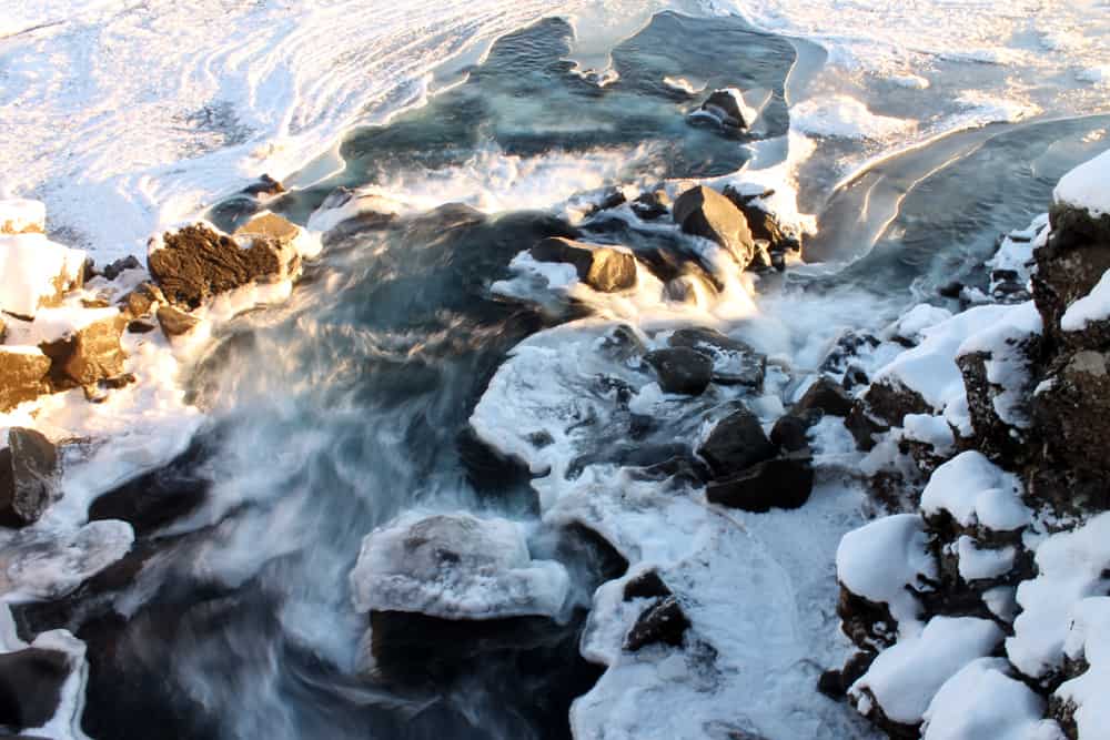Wasser bewegt sich durch einen gefrorenen Fluss mit Schnee