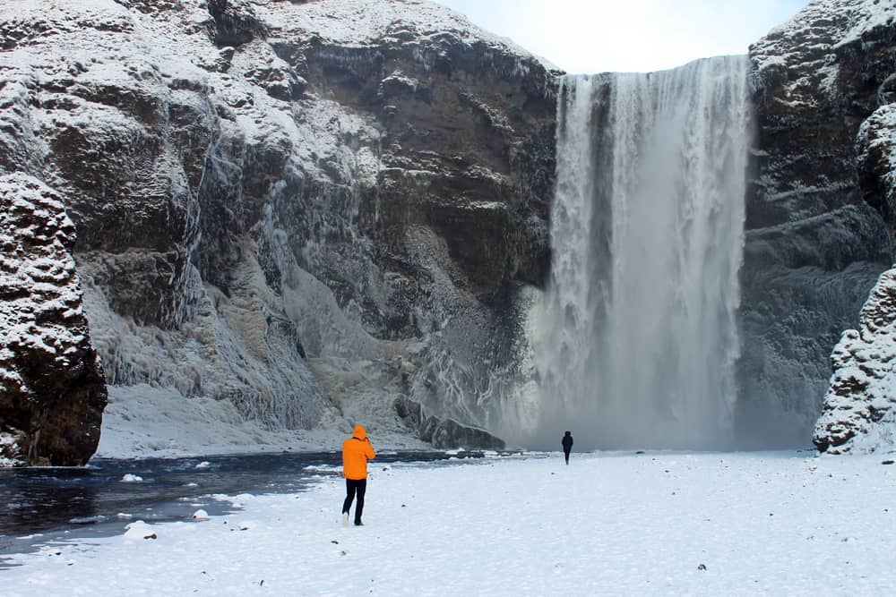 großer Wasserfall mit schneebedecktem Berg und zwei Personen