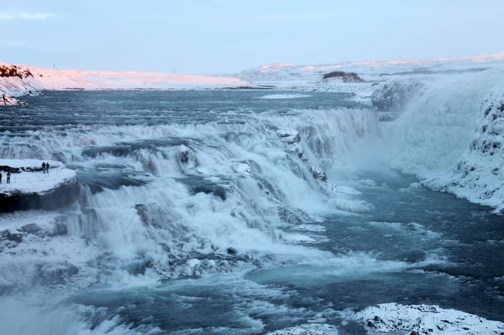 großer Wasserfall mit schneebedecktem Berg und zwei Personen