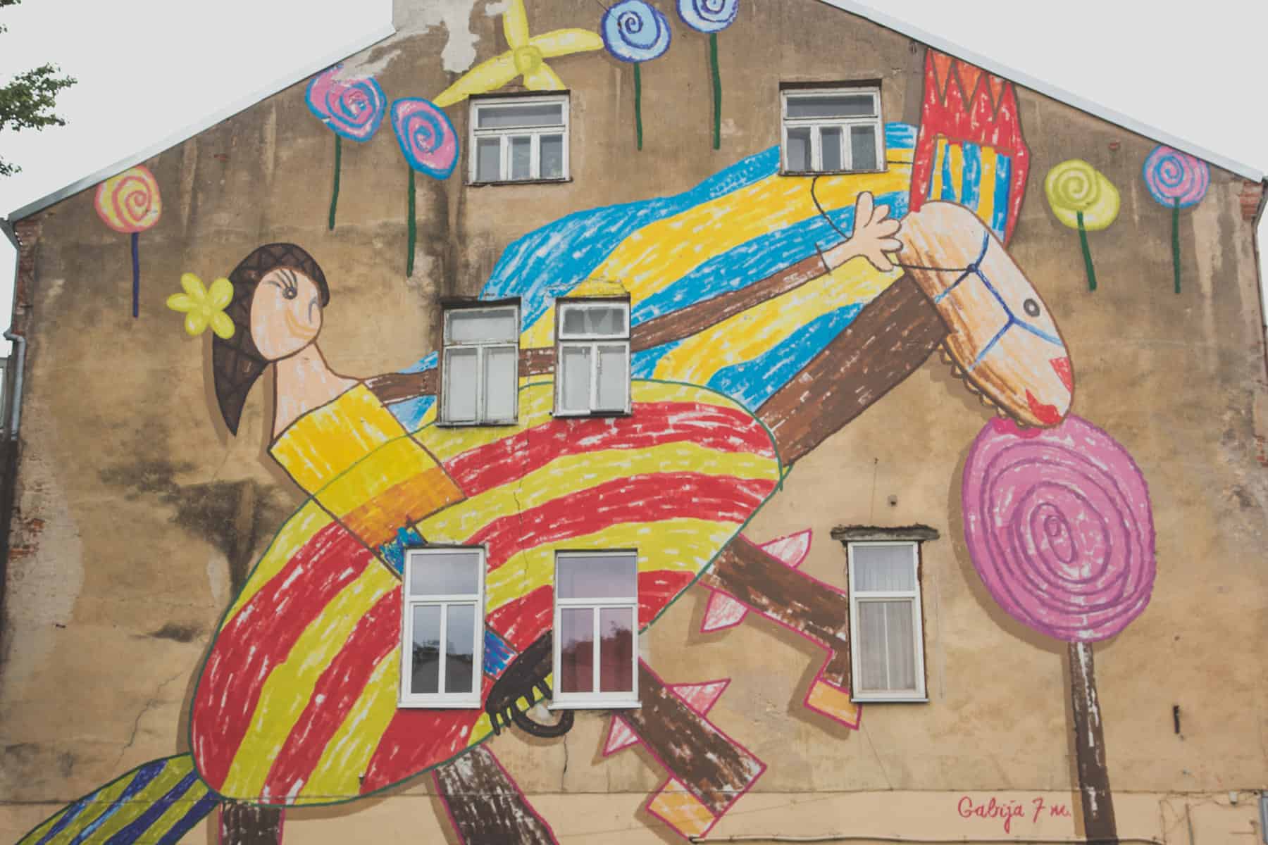 Kinderzeichnung auf einem ganzen Gebäude eines kleinen Mädchens, das auf einem Pferd reitet