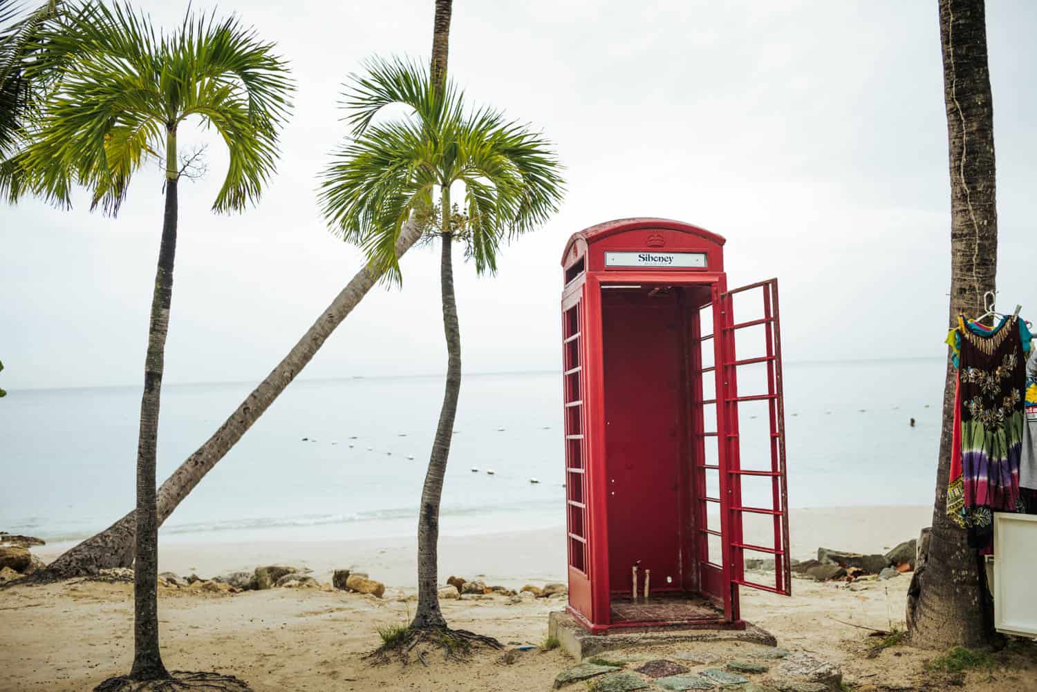 Rote Telefonzelle mitten am Strand mit Palmen