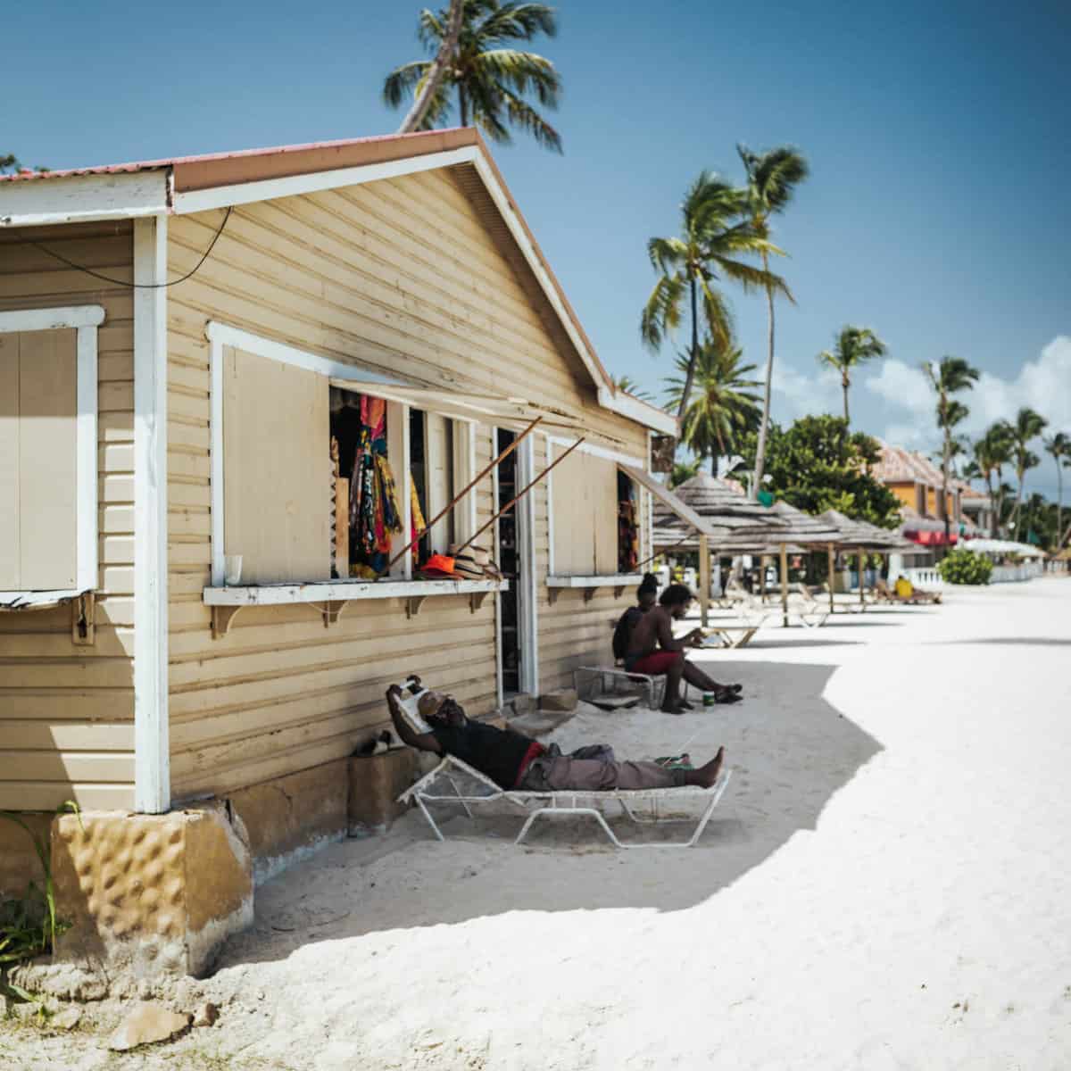 3 men relaxing on the beach with a tan building 