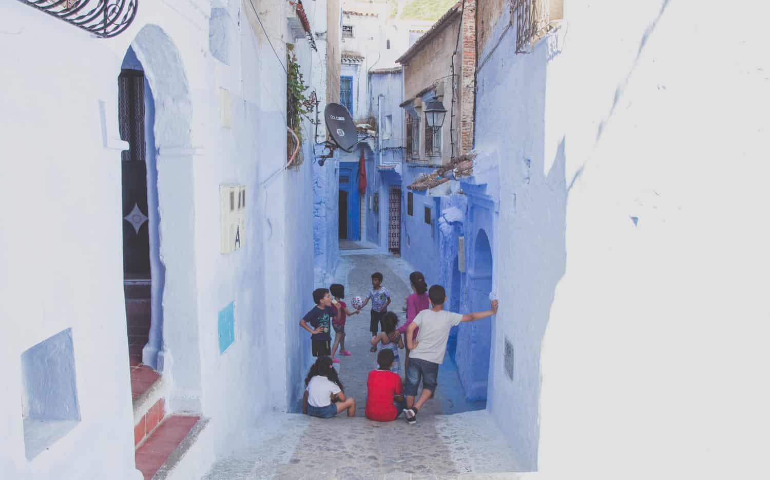 Kinder spielen mit einem Ball in einer kleinen Gasse mit blauen Gebäuden in Marokko