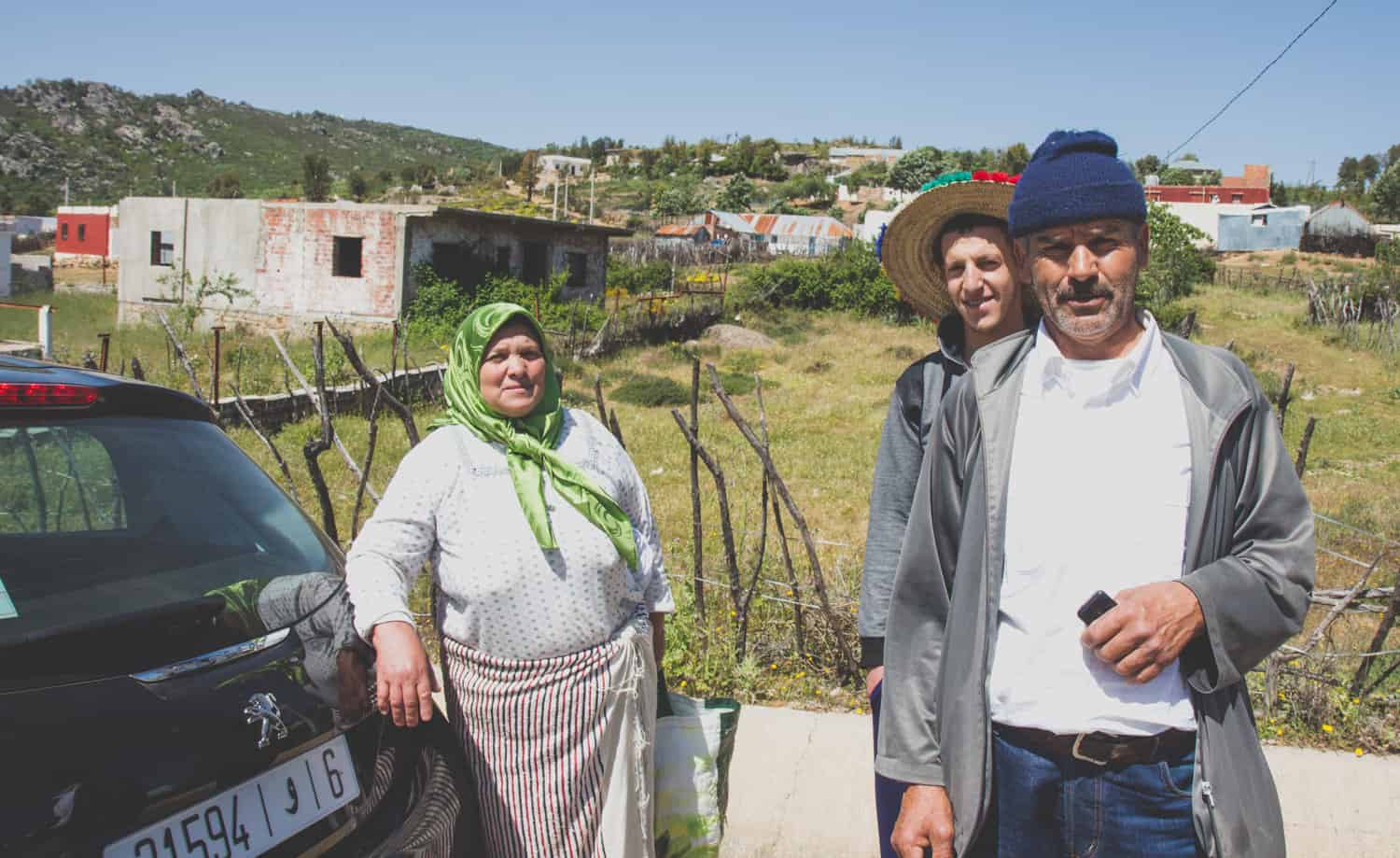 3 einheimische Marokkaner auf einer Dorfstraße neben einem Auto, das auf einer Marokko Reise erbeutet wurde