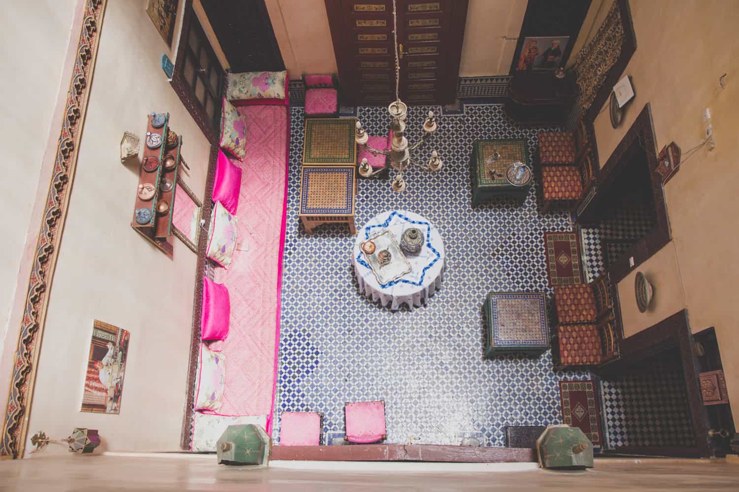 Bild von oben eines kleinen Esszimmers mit Tischen, blauen Fliesen und rosa Kissen