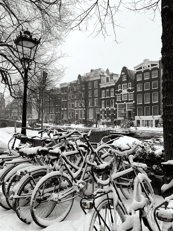 Amsterdam Bikes covered in snow with Amsterdam Canal Houses in the background