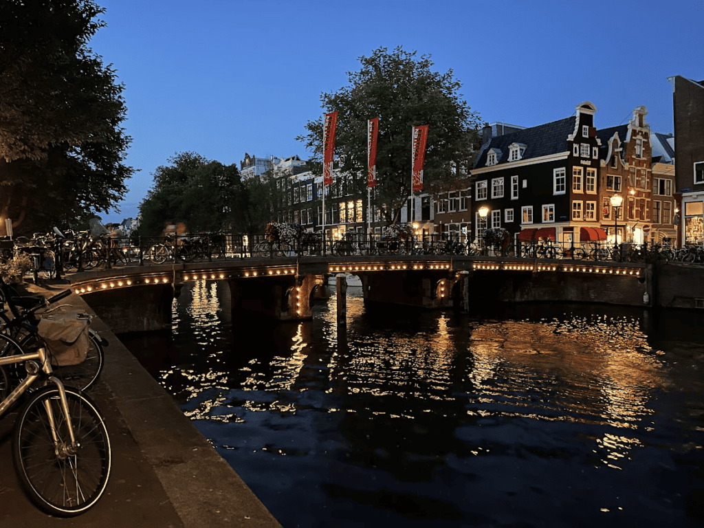 Amsterdam Canal Houses at night over lite bridge with bicycles and trees