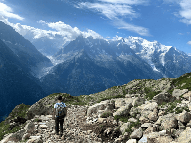 Hiker walking along Tour du Mont Blanc Trail with Snow covered Alps Mountain Range in the background