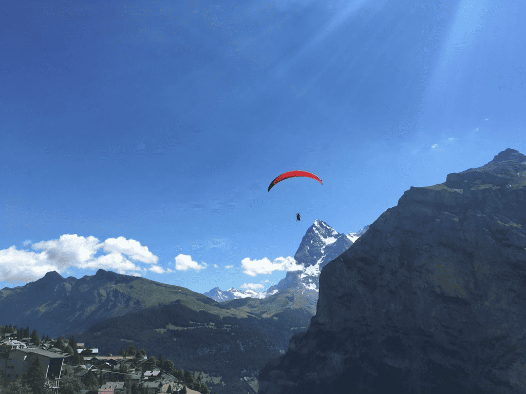 Red paraglide shown paragliding in Switzerland over the Alps with snow covered mountains and rocks