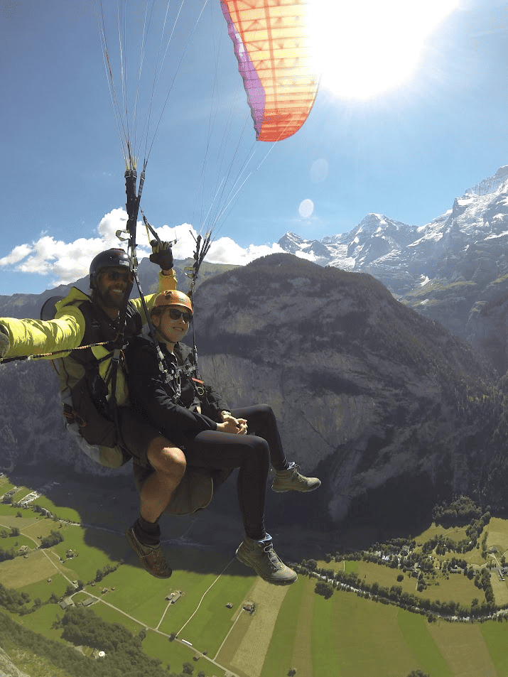 Girl and Guide shown smiling while paragliding in Switzerland with snow covered mountains