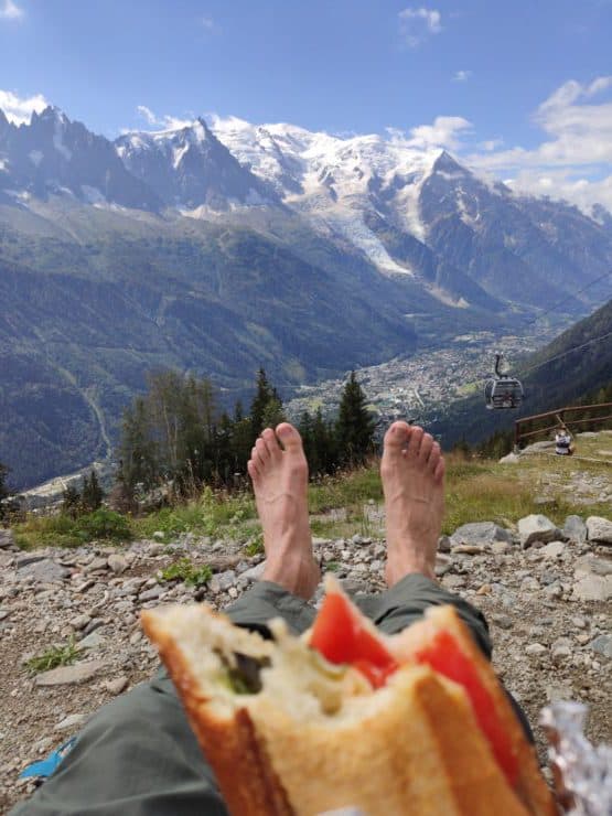 Snow covered Alps Mountain Range in the background with a sandwich and hiking feet