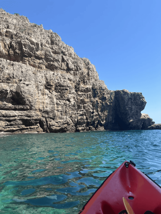 Red Kayak on a blue water with jagged rock behind