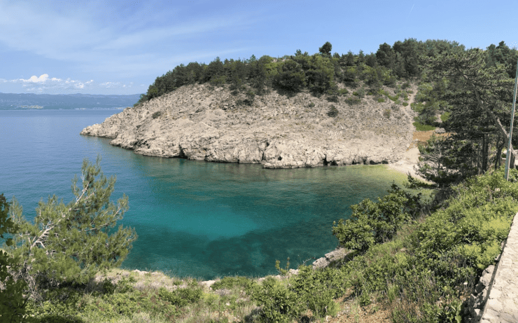 Secluded beach with blue waters, and a plant covered cliff on a Croatia Vacation Roadtrip