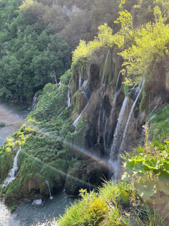 Waterfalls cascading with a rainbow and greenery at Plitvice Lakes National Park