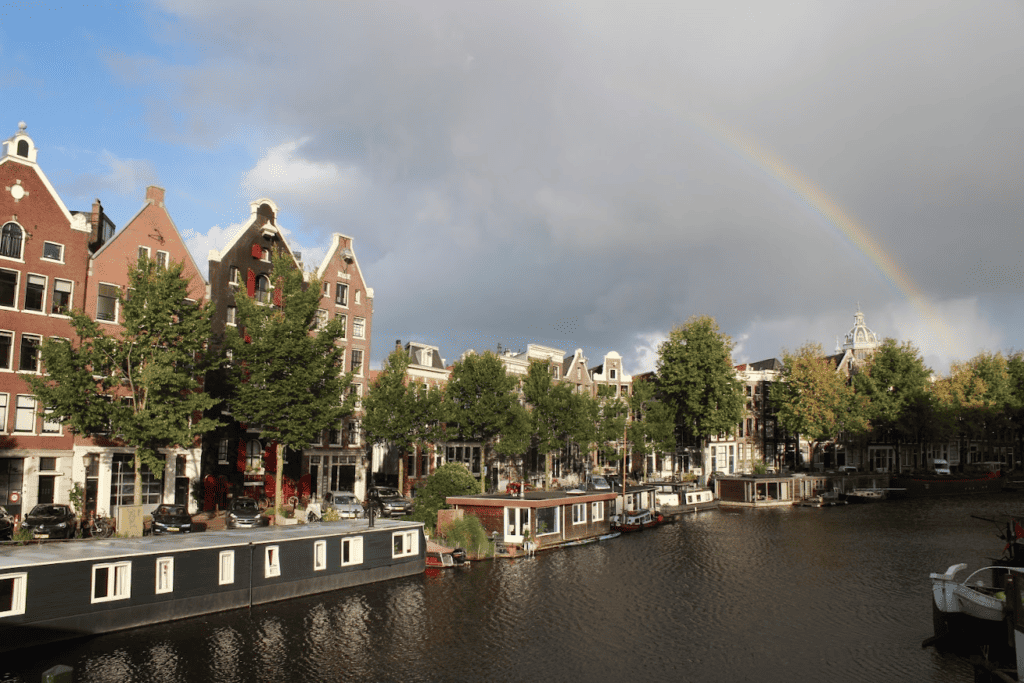 Alte Kanalhäuser und eine Brücke spiegeln sich über dem Wasser in Amsterdam mit einem Regenbogen
