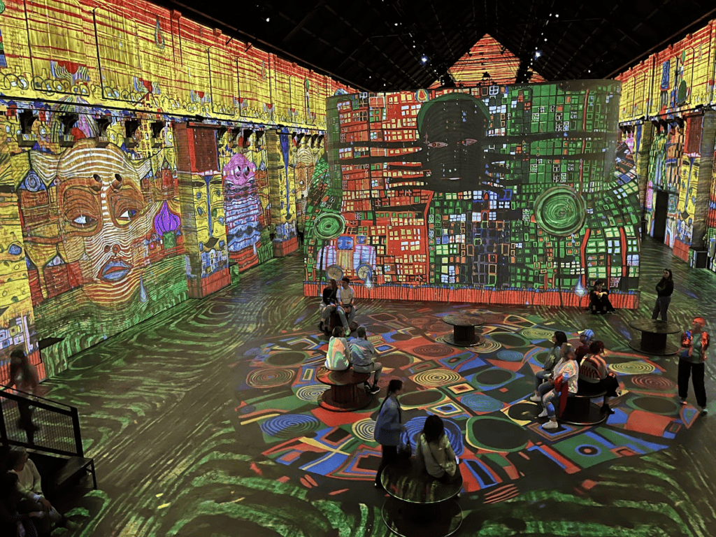 Colorful modern art with faces is projected on the walls and floors at Fabrique des Lumieres