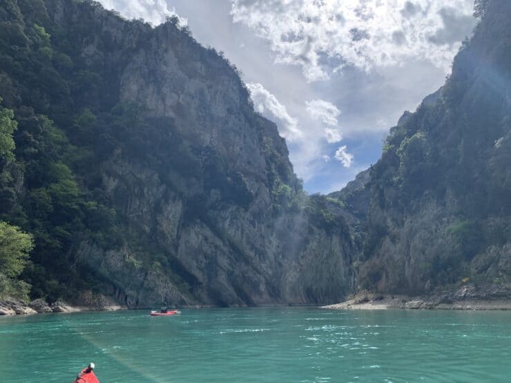 red kayak on crystal blue waters with large rocks and blue sky