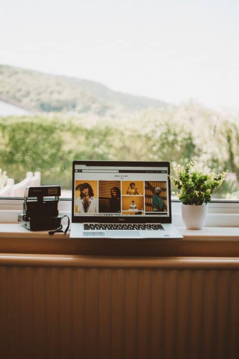 A Laptop and a Polaroid on a Wooden Table Beside a Pot of Flowers