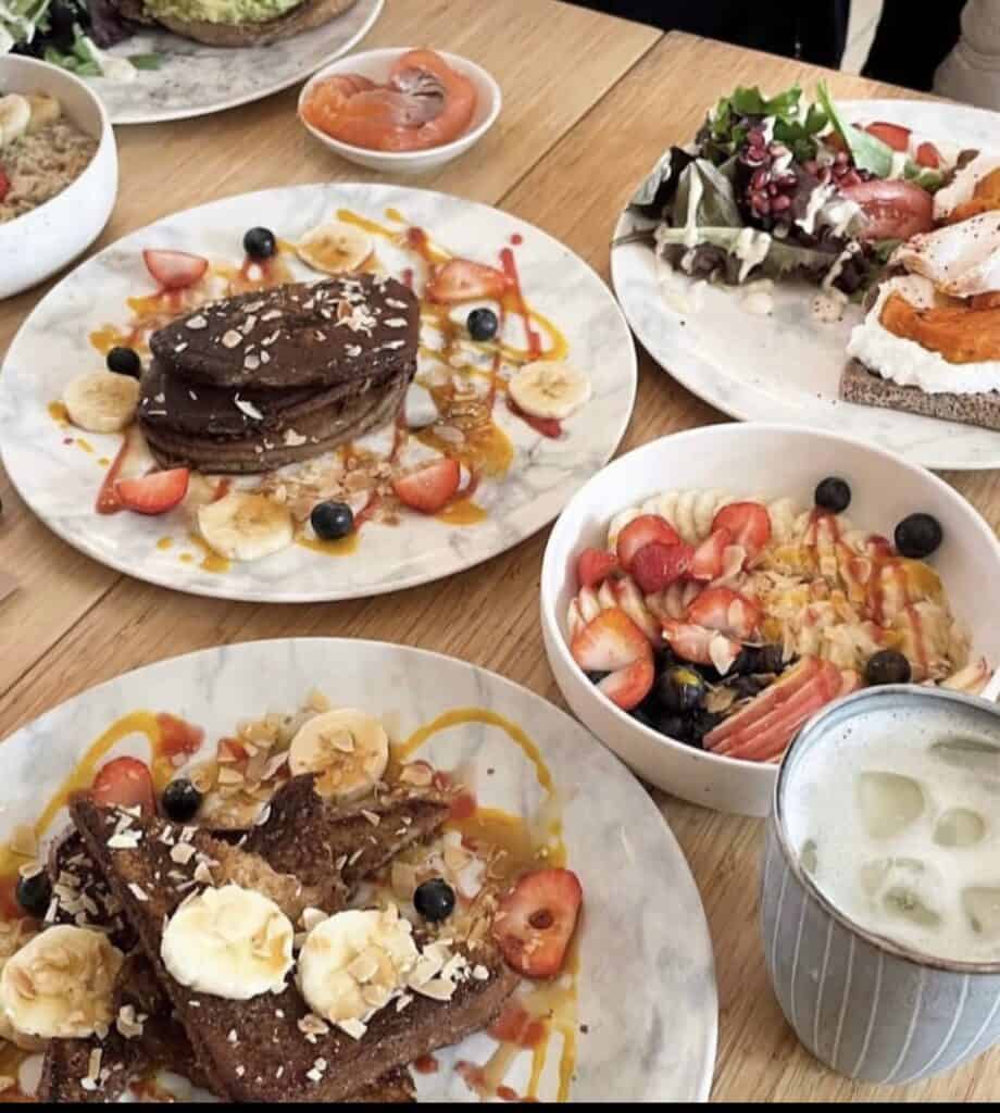 Various plates of brunch foods with pancakes, smoothie bowl, french toast and a drink all artfully decorated at Lavinia Good Food