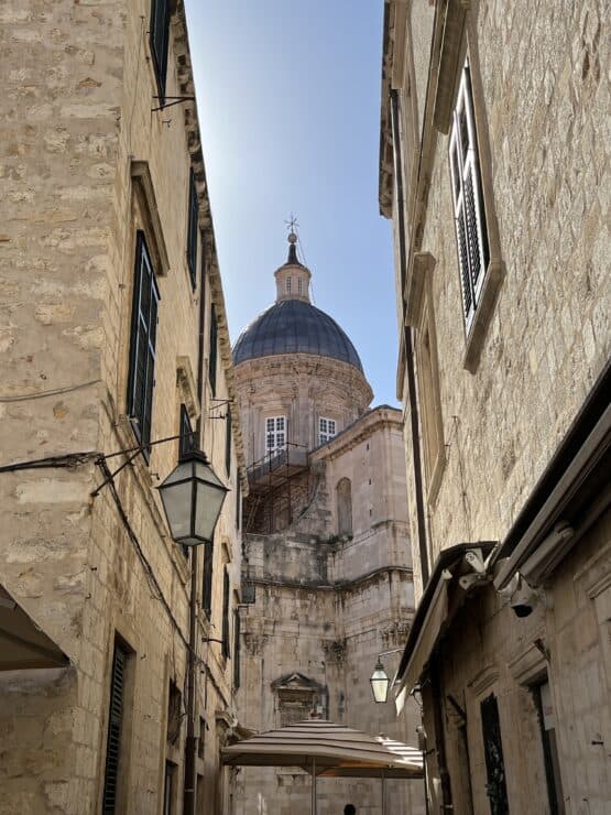 Old stone buildings frame a domed building in Dubrovnik with a blue sky