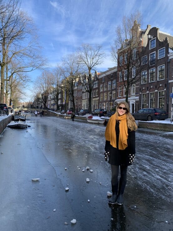 Smiling women stands on a frozen canal with canal houses behind her in Amsterdam