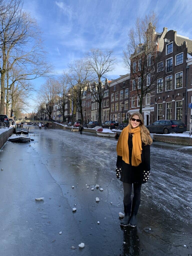 Frauen mit gelbem Schal lächeln auf einem zugefrorenen Kanal mit Grachtenhäusern in Amsterdam